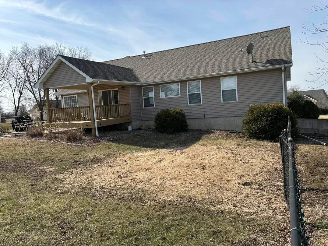 Tan house with wooden deck on a grassy hill under a blue sky.
