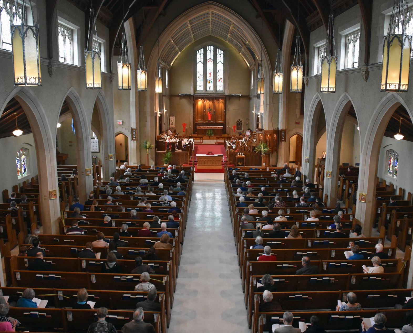Interior of a church with rows of people in pews facing the altar and stained glass windows.