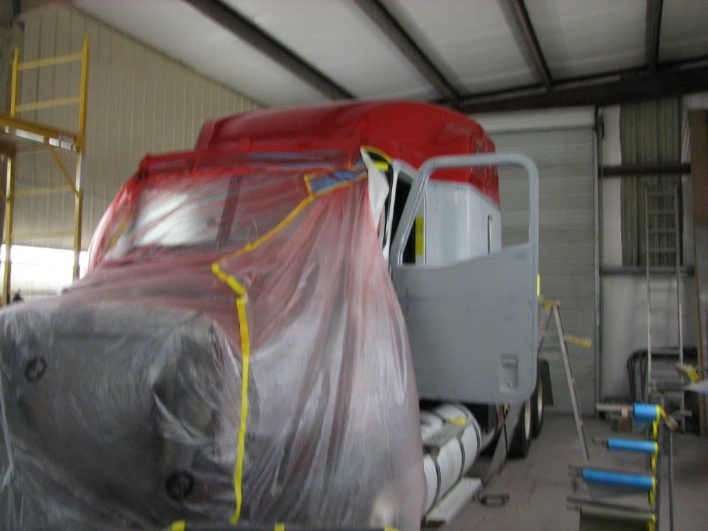 A red truck is covered in plastic in a garage