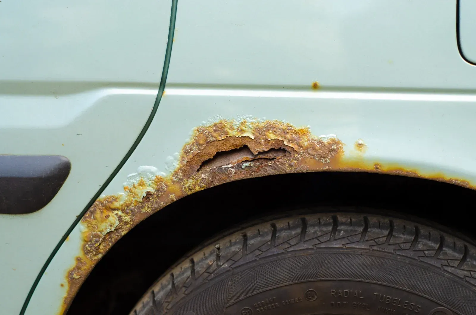 A close up of a rusty car fender and tire.