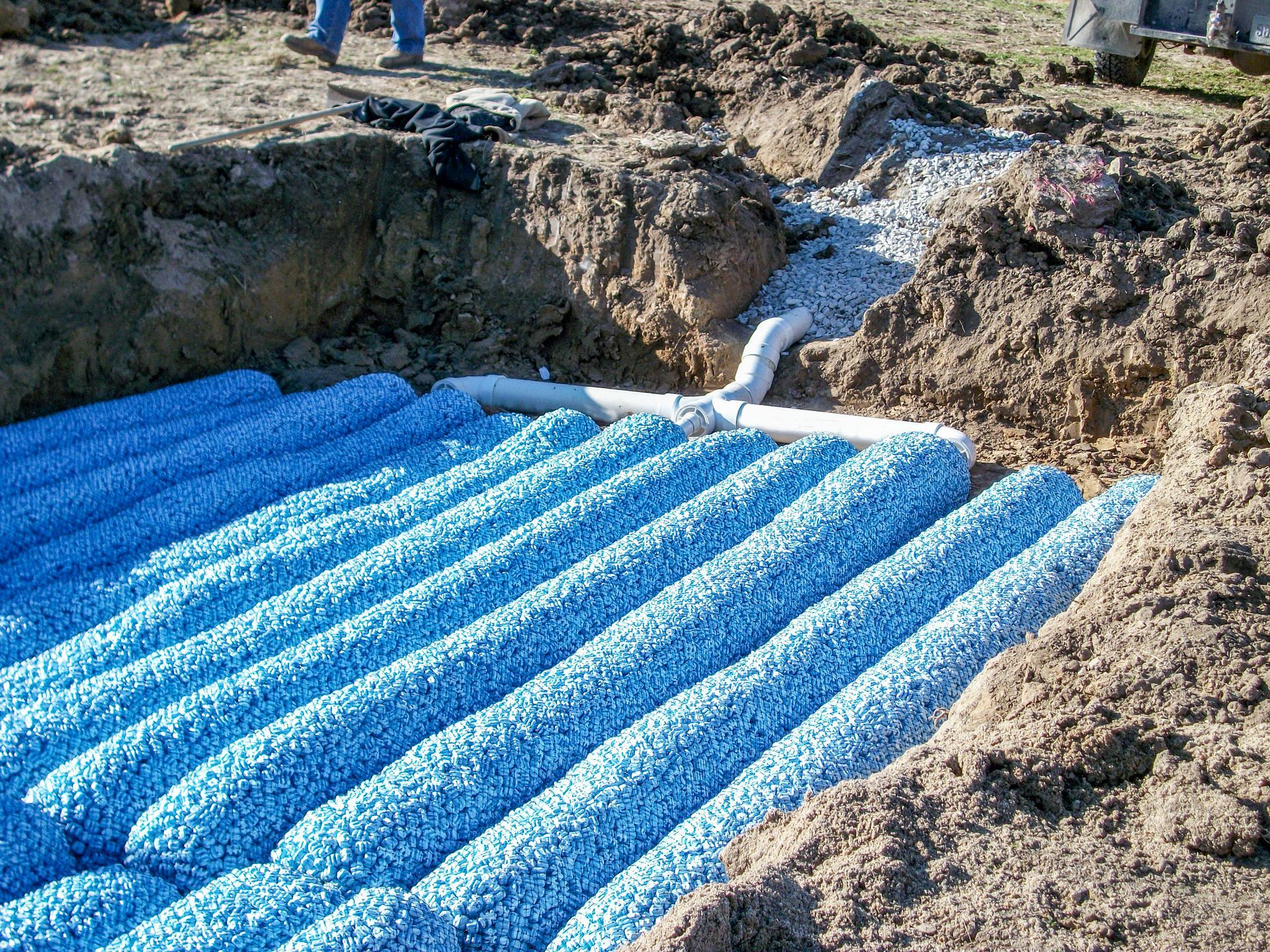 Blue drainage pipe installed in a muddy excavation site with water flowing in.