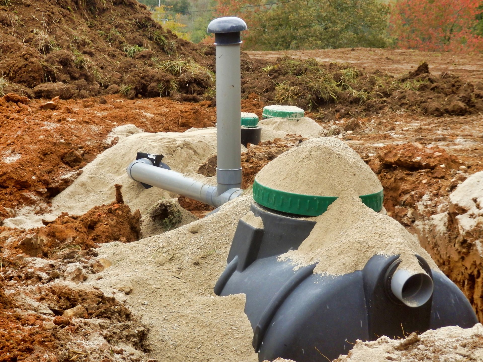 Septic tank installation with gravel-filled underground pipes and vents at a construction site