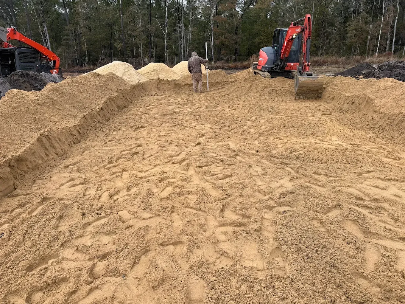 Dirt construction site with two excavators and a worker on a large sandy mound