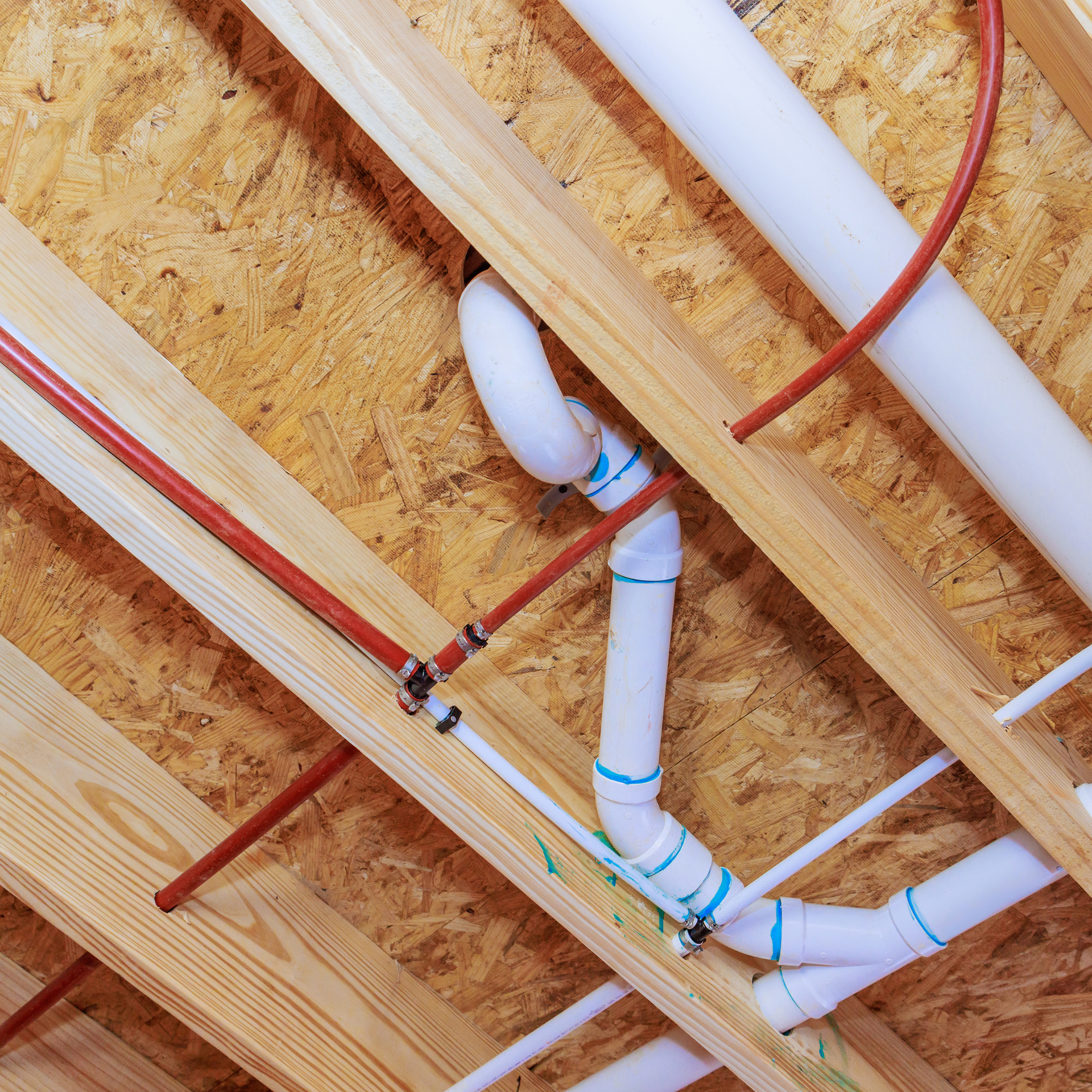 Pipes and plumbing, with red and white pipes secured to wood beams in a building’s ceiling.