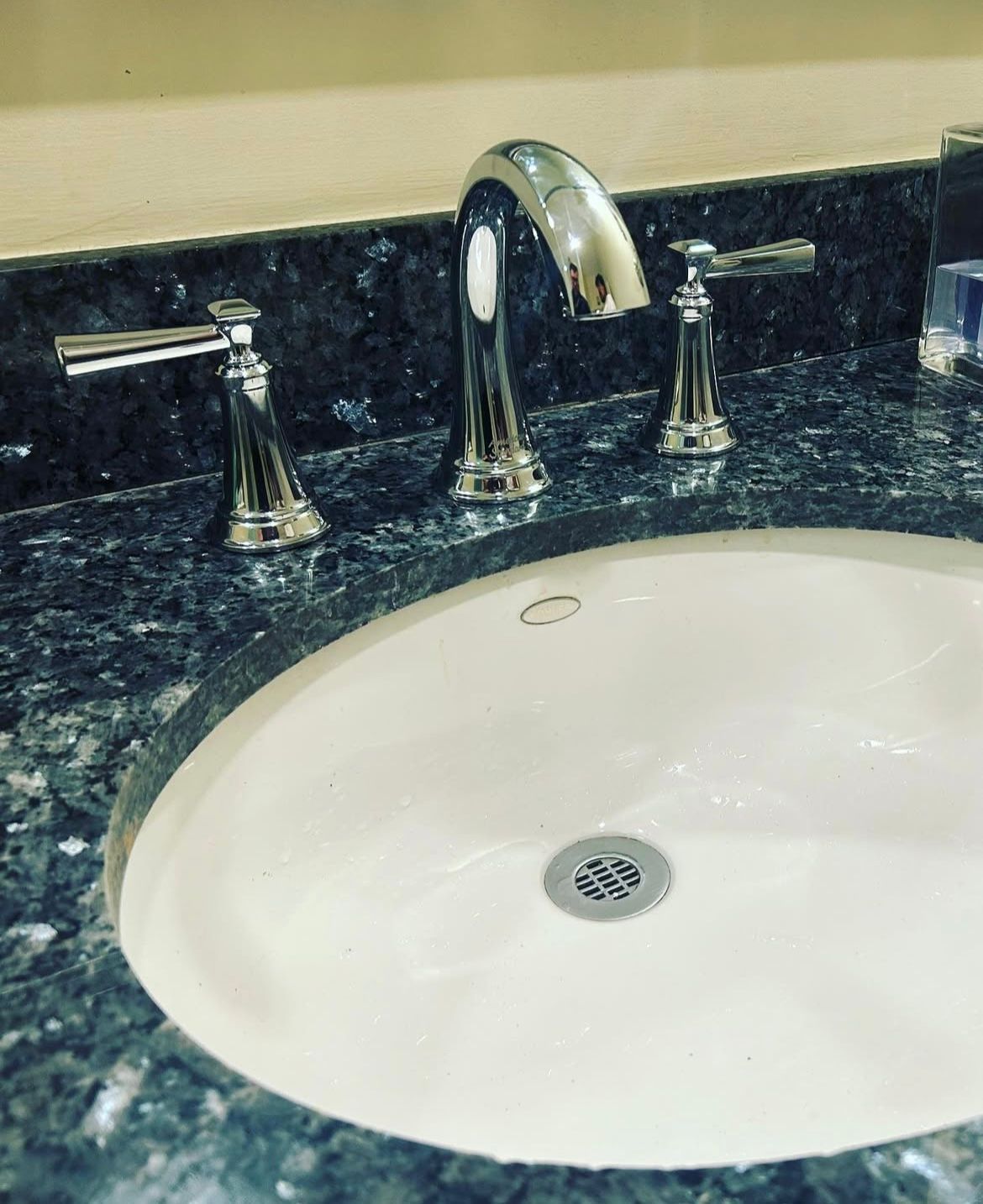White oval sink with chrome faucet and handles on a blue speckled countertop.