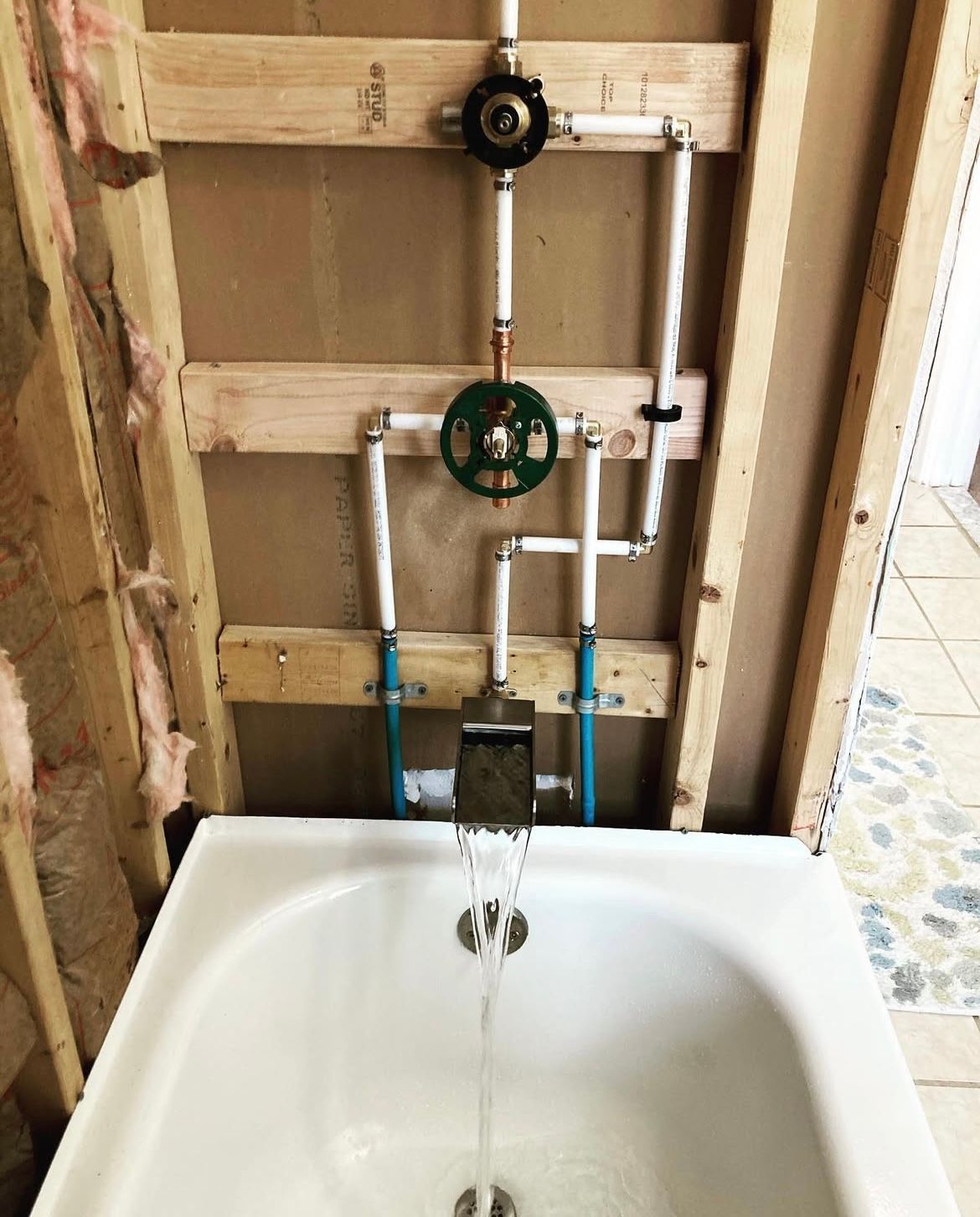 Tub with exposed plumbing in a partially constructed bathroom; white tub, white pipes, and green valve.
