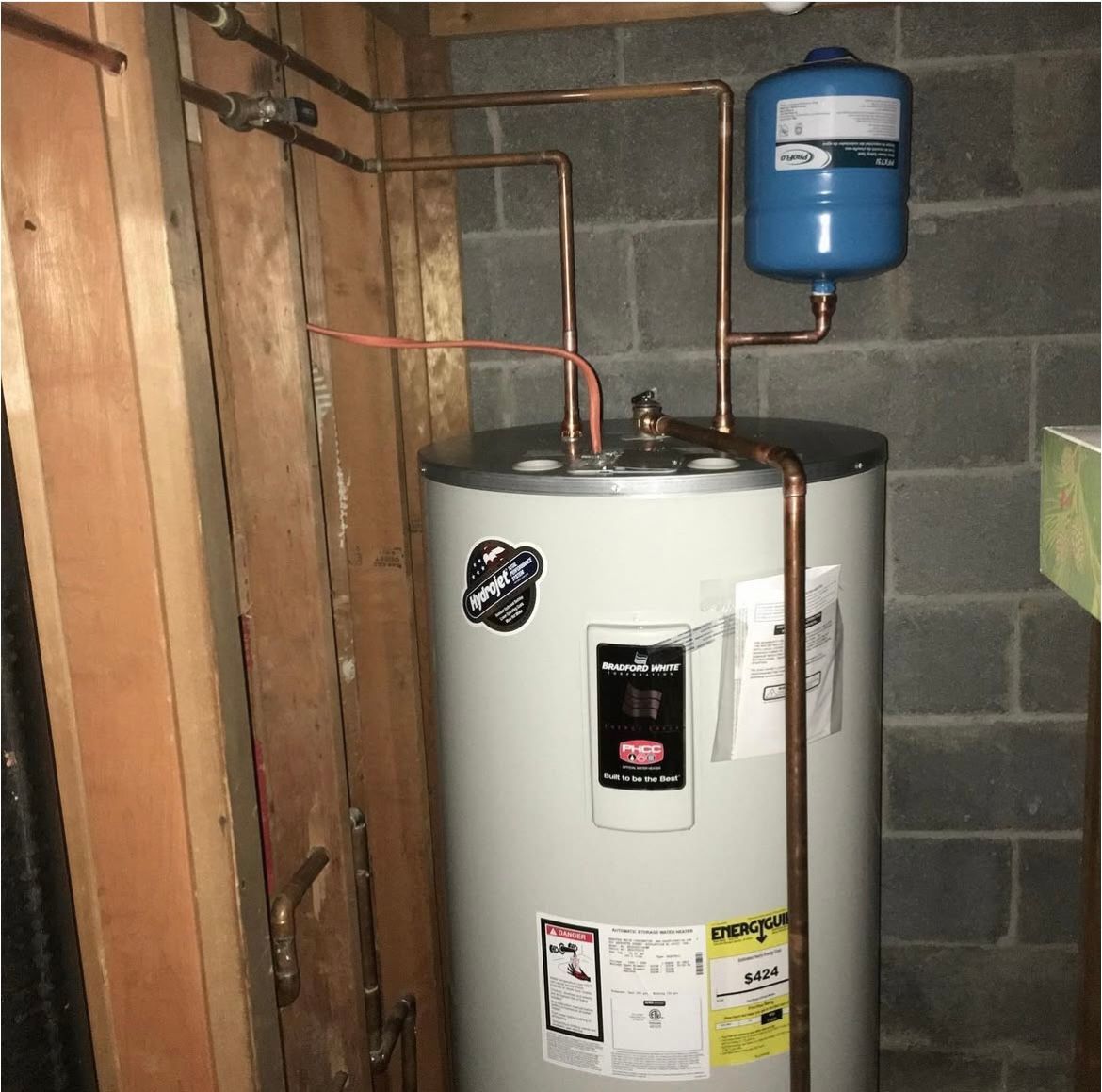A water heater with copper pipes, and an expansion tank in a basement.