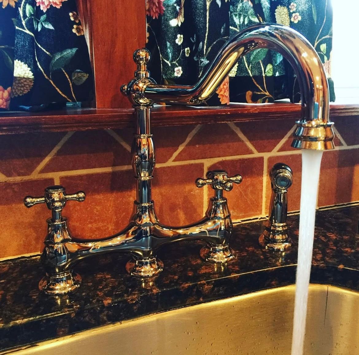 Chrome kitchen faucet with water flowing into a sink, against a patterned backsplash.