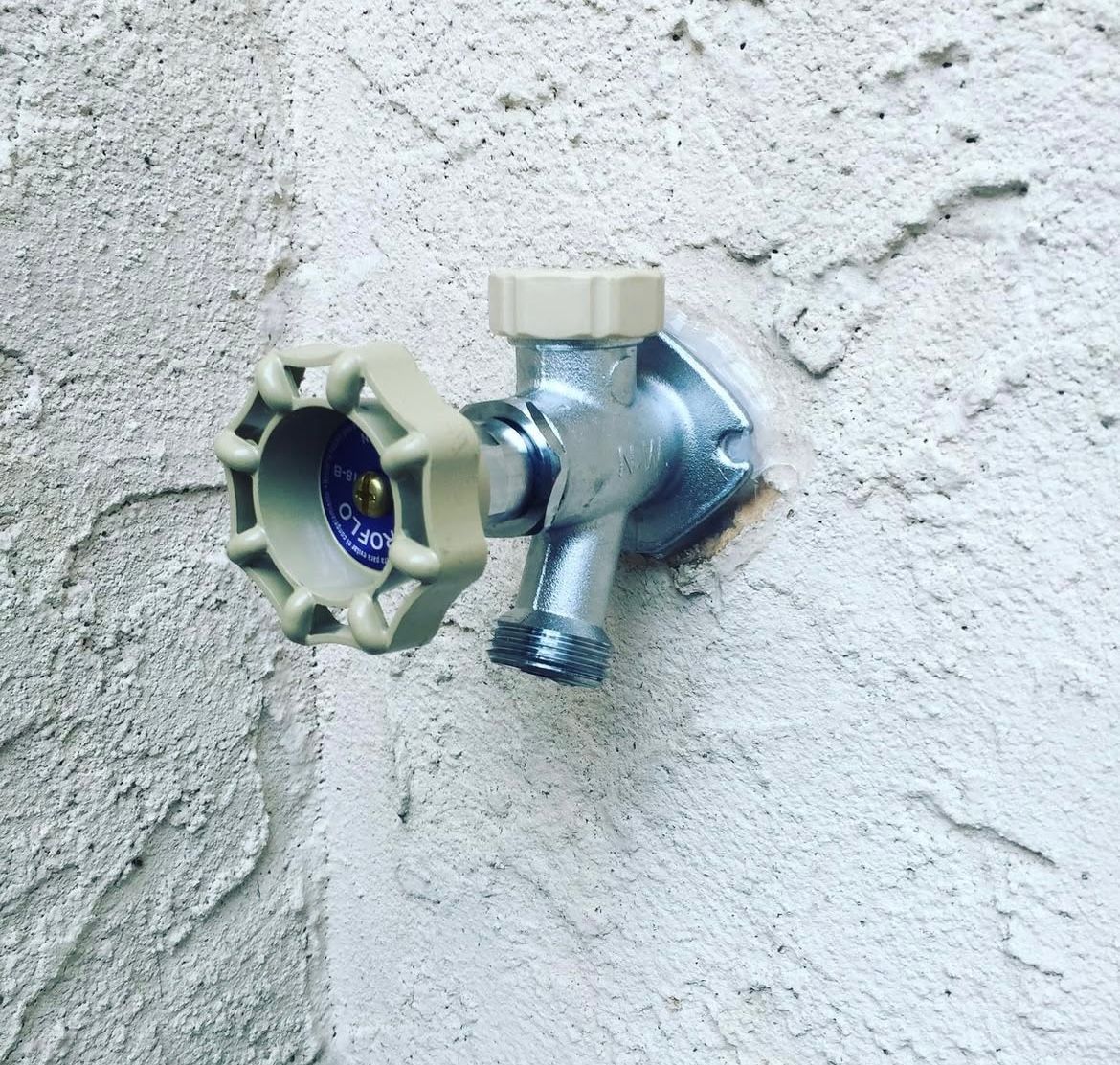 Outdoor water faucet on a textured white stucco wall.