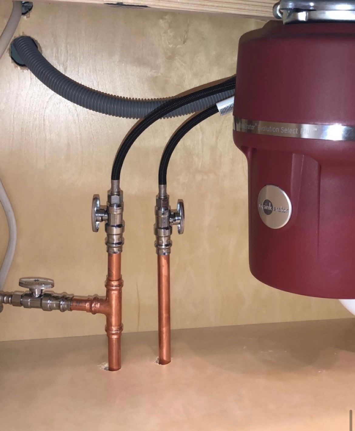 Copper pipes with shutoff valves under a kitchen sink, next to a garbage disposal.