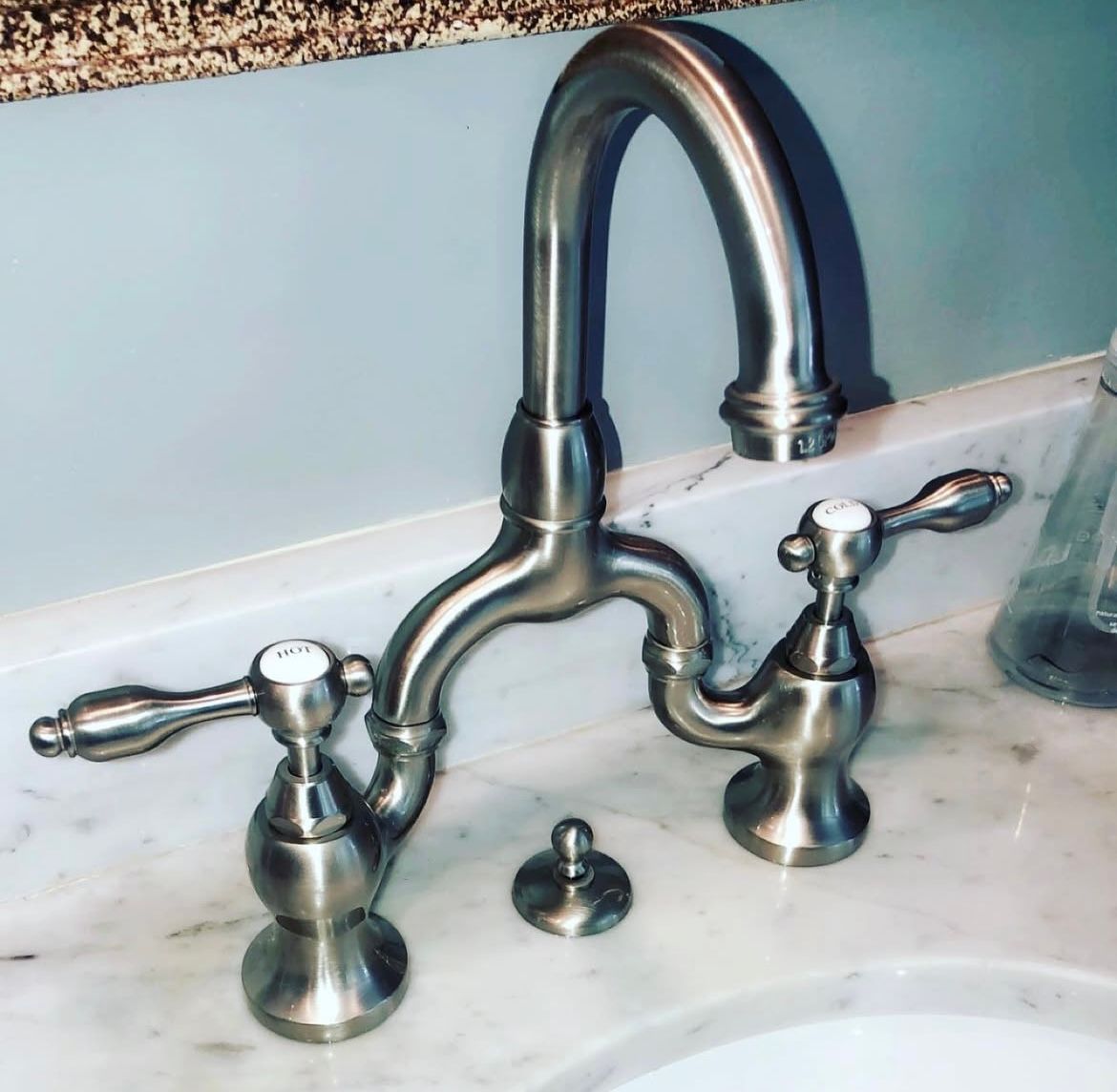 Brushed nickel bathroom faucet with two handles and a central spout, on a marble countertop.