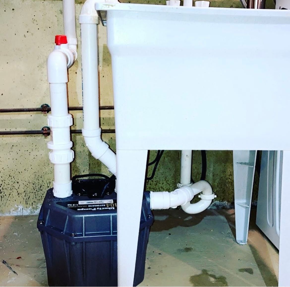 Laundry sink with connected pipes and a pump in a basement.