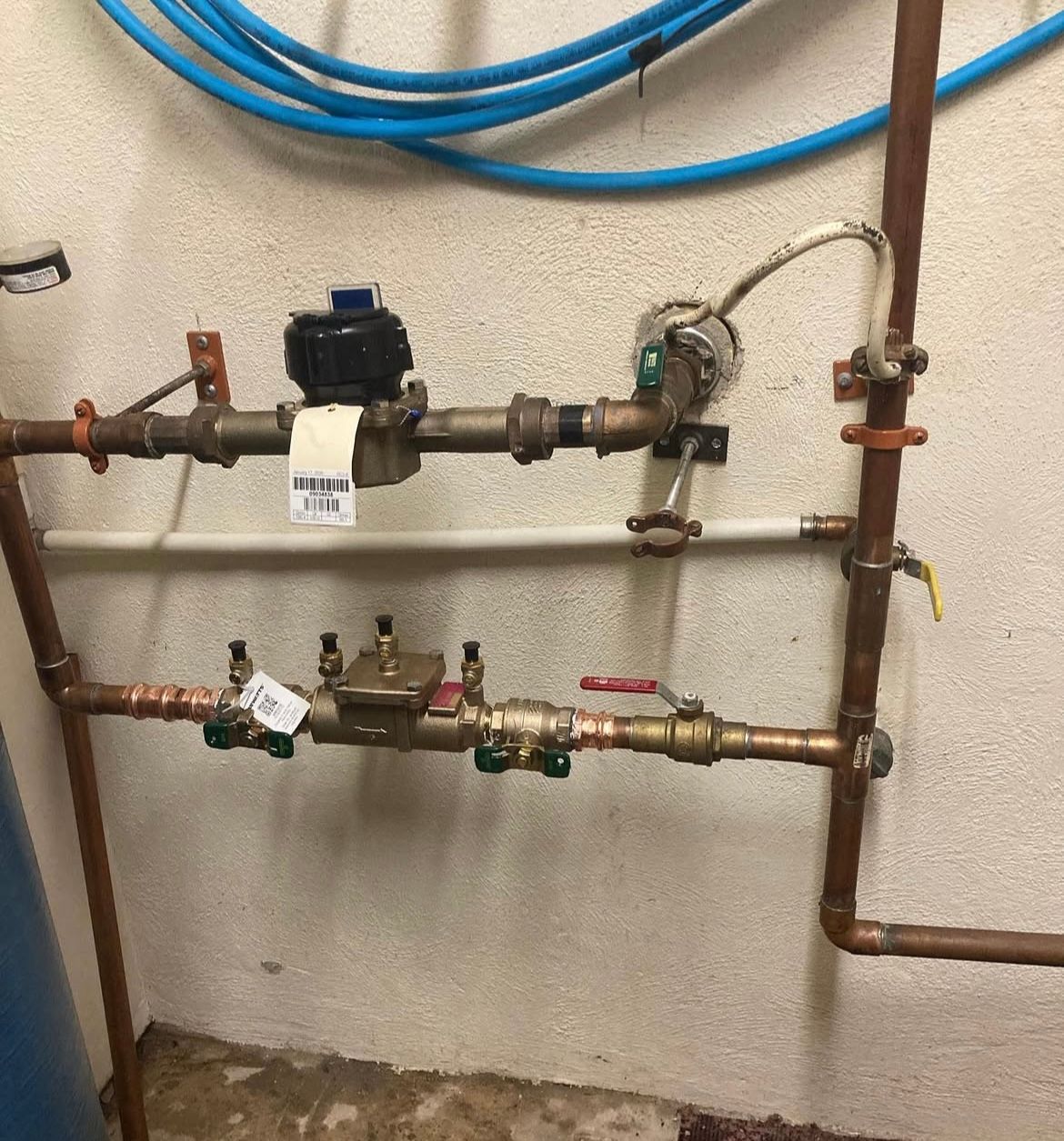 Copper pipes and valves against a beige wall; includes a water meter and pressure regulator.