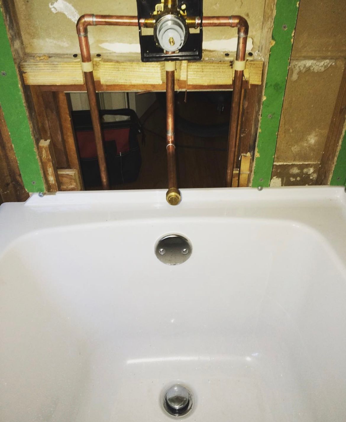 Plumbing installation for a bathtub; copper pipes connected to a valve set above the tub.