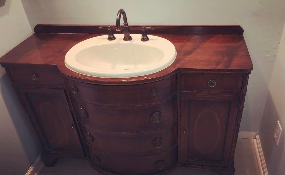Wooden bathroom vanity with a white sink and dark faucet against a blue wall.