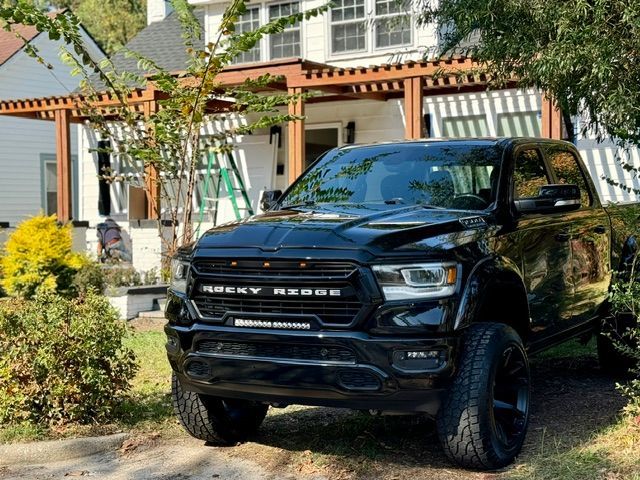 Black Ram pickup truck parked in a front yard beside a house with a pergola and shrubs.