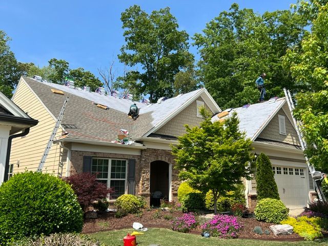 Suburban house with beige siding, white roof, and landscaped front yard under a blue sky