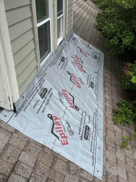 Roofing underlayment on a small sloped porch roof beside a house and brick walkway