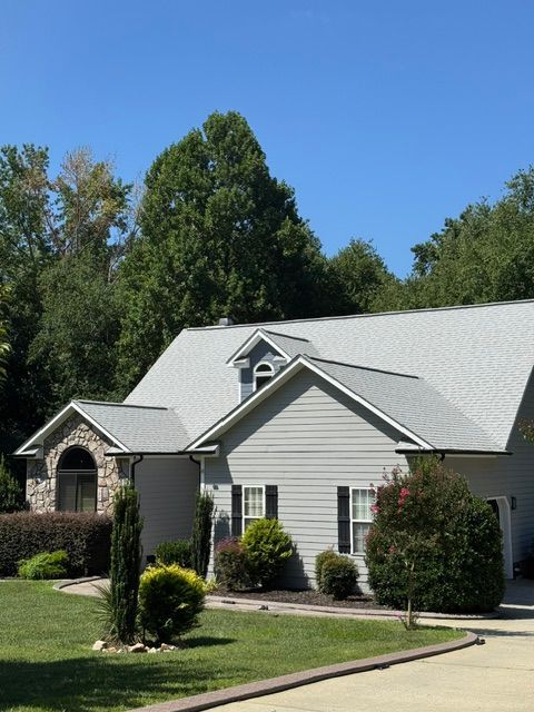Suburban house with white siding, gray roof, and landscaped green lawn under a clear blue sky