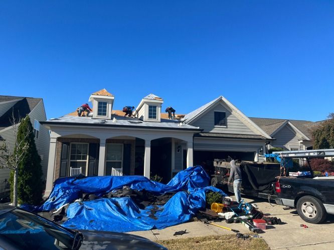 House exterior with blue tarps, construction debris, and a pickup truck in the driveway under a clear blue sky