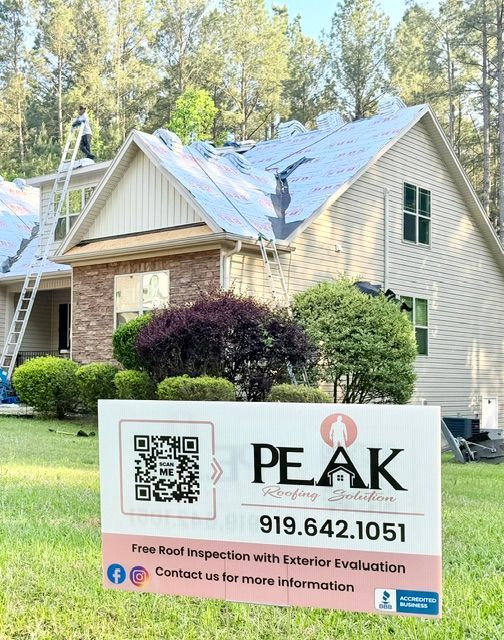 Home exterior with a PEAK roofing sign in front of a house and trees