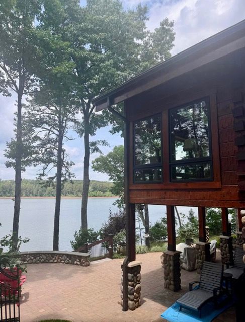 Lakeside cabin deck with stone columns, trees, and a calm lake view at sunset