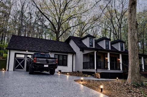Black-and-white modern farmhouse with black truck parked on gravel driveway at dusk