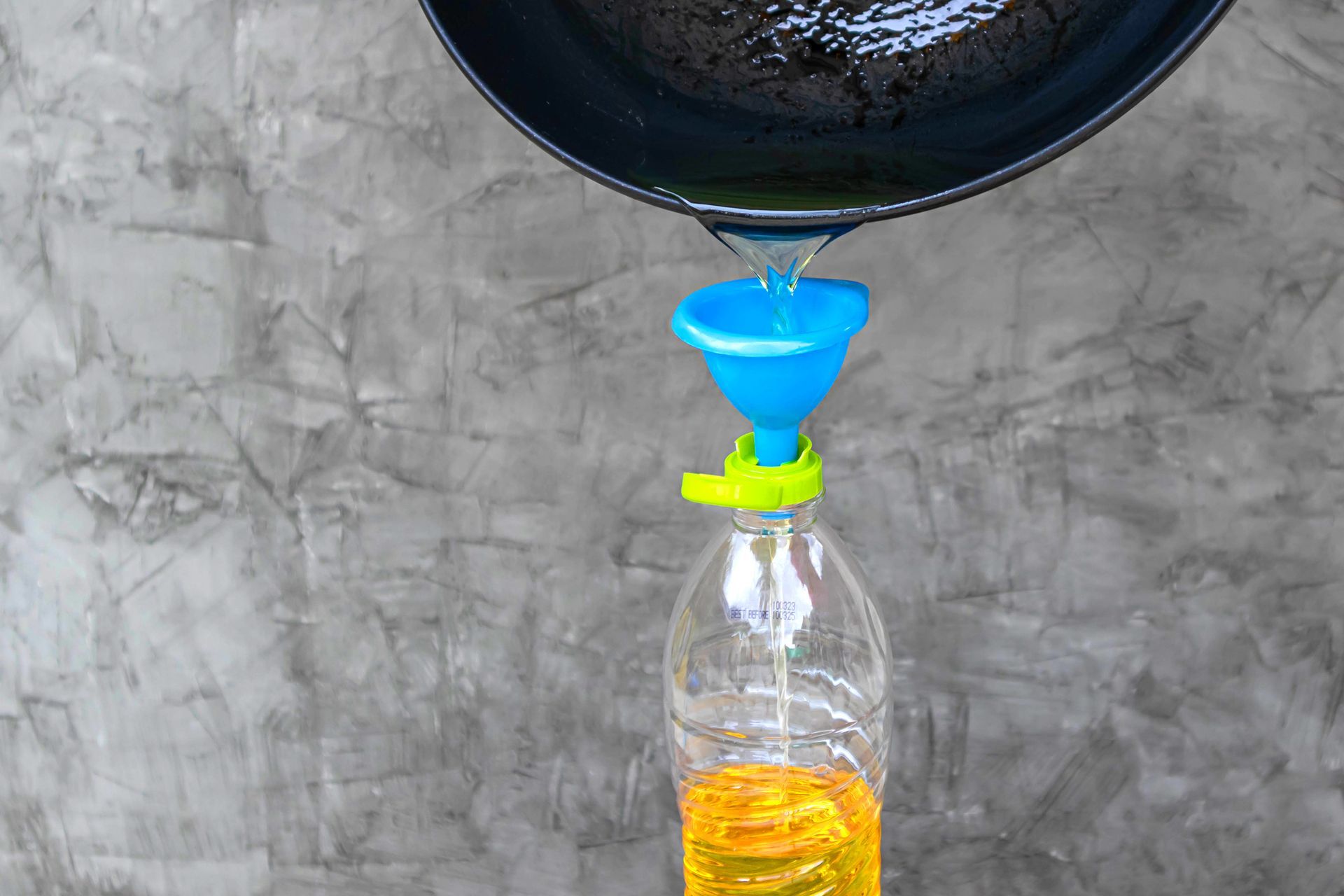 Pouring used cooking oil from the pan into a plastic bottle. Pouring used cooking oil from the pan into a plastic bottle.