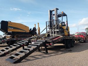 A forklift is on a trailer with ramps attached to it.