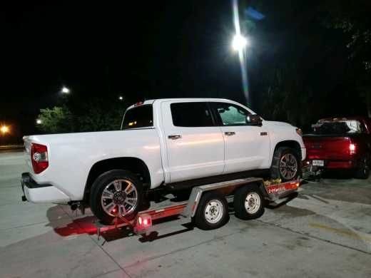 A white truck is being towed by a trailer.