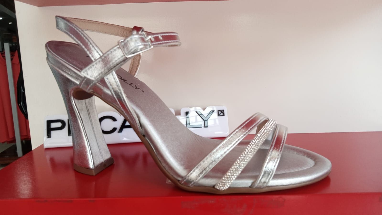 Sandalia de tacón alto plateada sobre plataforma roja, con tira fina en el tobillo y múltiples tiras sobre los dedos.