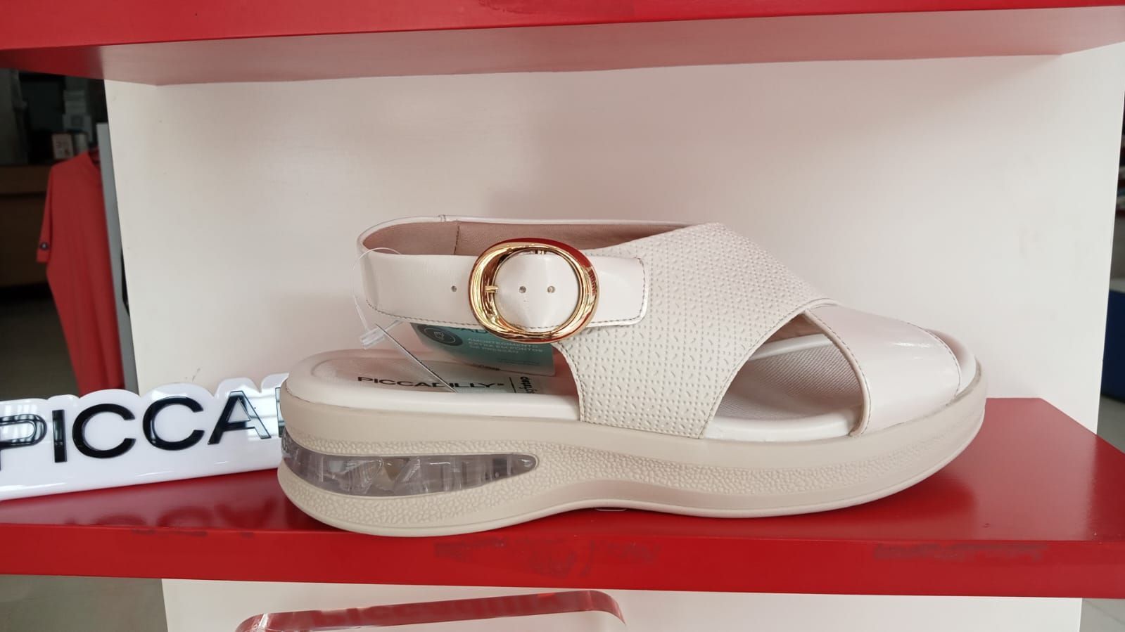 Sandalia blanca con hebilla dorada en el estante de una tienda.