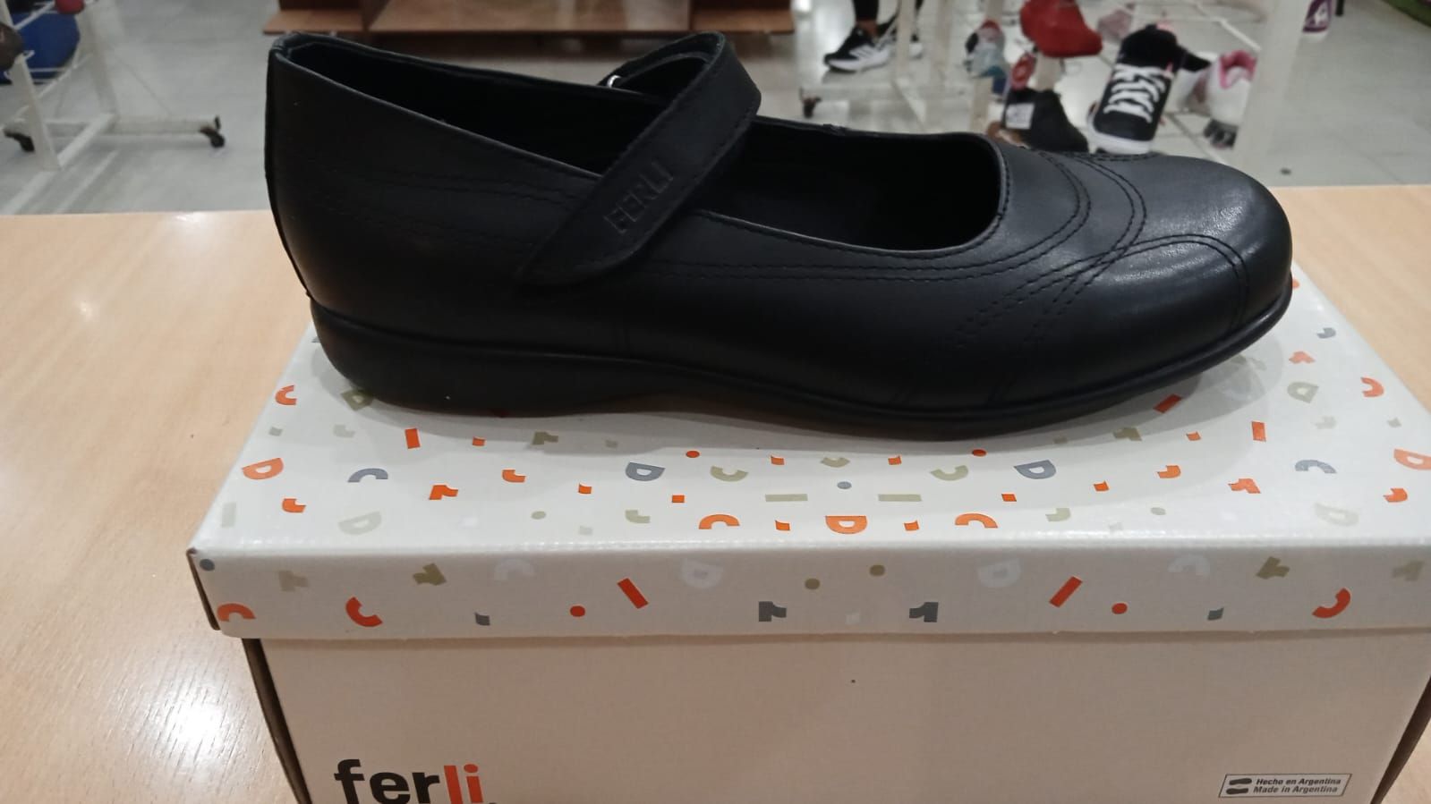 Zapato negro sobre una caja de zapatos blanca con diseños coloridos, sobre una mesa de madera.