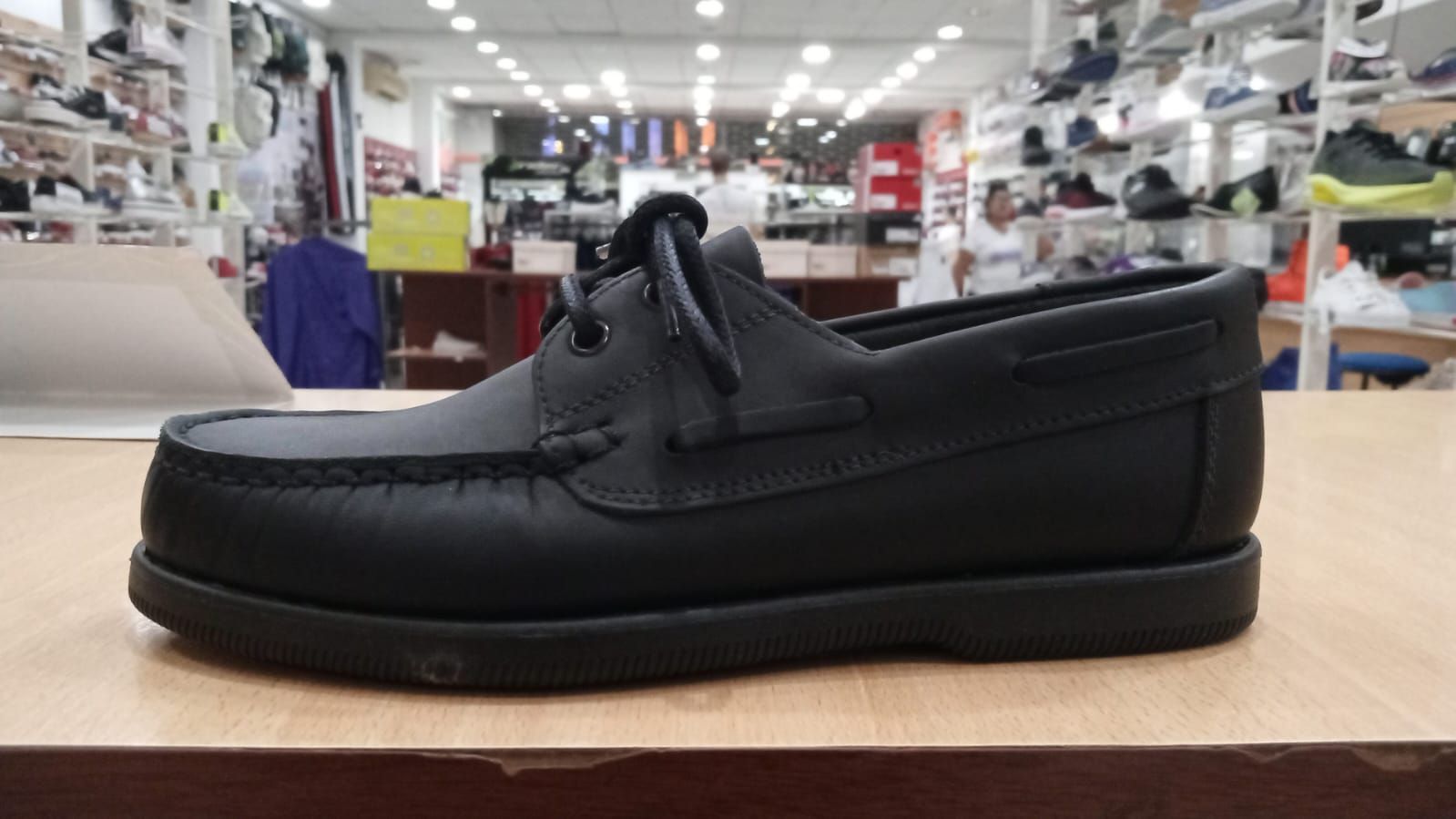 Zapato náutico de cuero negro sobre una superficie de madera en una zapatería.