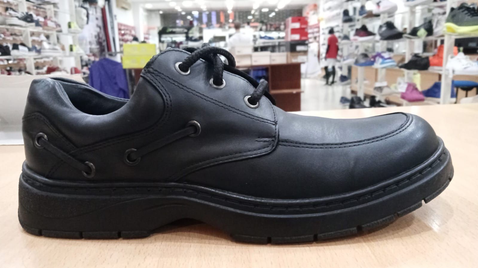 Zapato de piel de color negro, con suela gruesa, con cordones, sobre una superficie de madera en una zapatería.