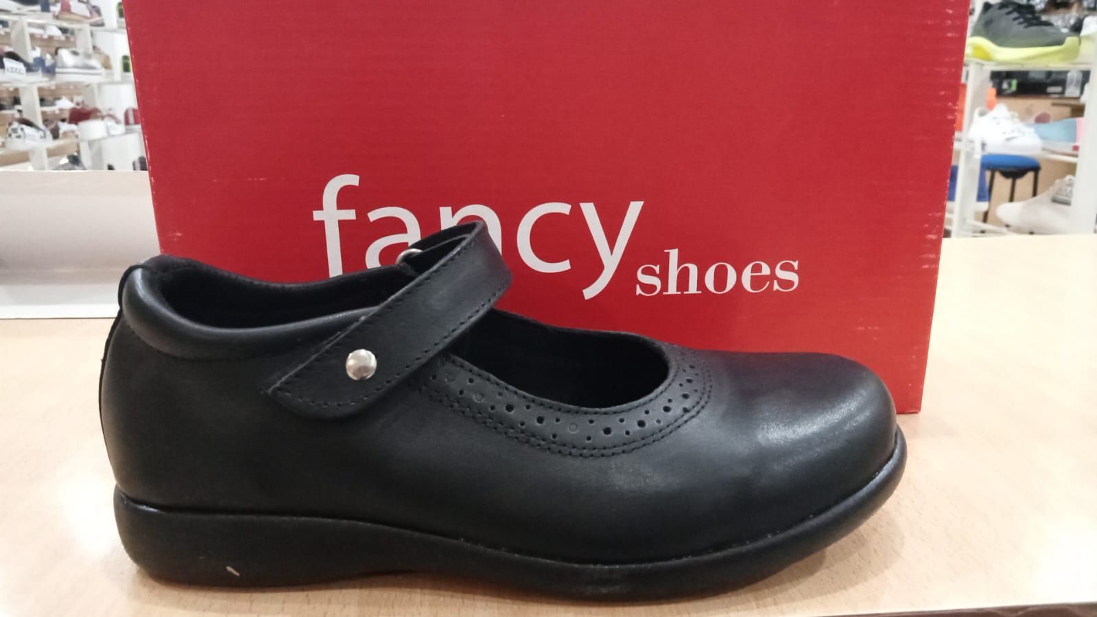 Zapato Mary Jane de color negro con correa, delante de una caja roja con la etiqueta 