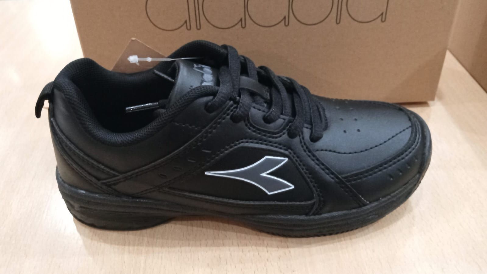 Zapatilla deportiva Diadora de color negro con logotipo blanco y una caja de zapatos marrón de fondo.