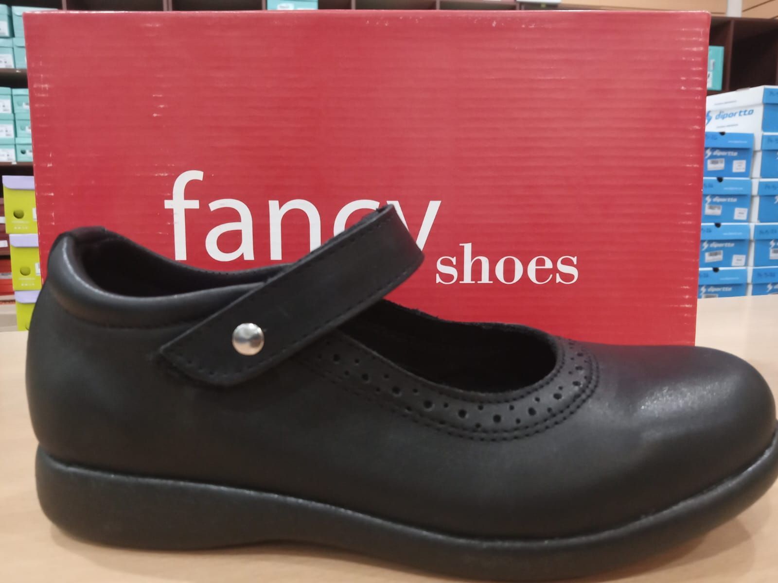 Zapato negro estilo Mary Jane exhibido frente a un letrero rojo de Fancy Shoes.