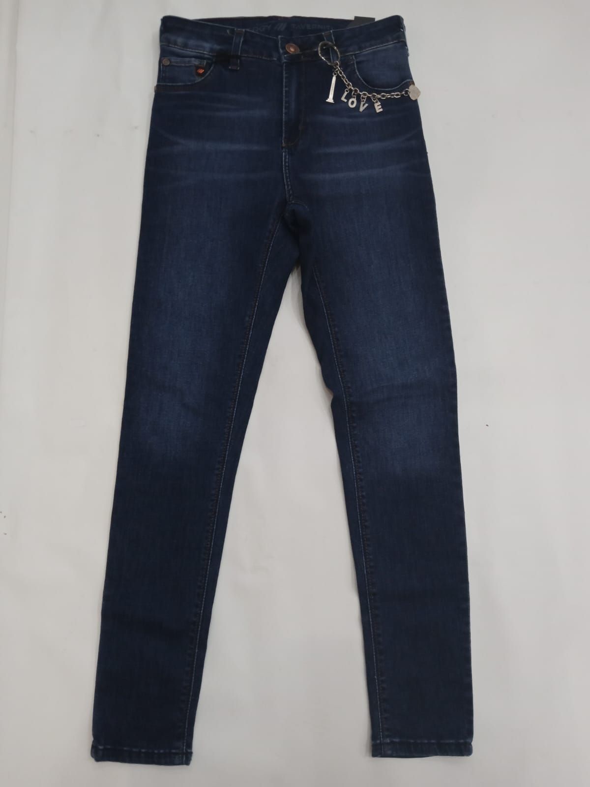 Pantalones vaqueros azul oscuro con detalle de cadena en la cinturilla, colocados sobre un fondo blanco.