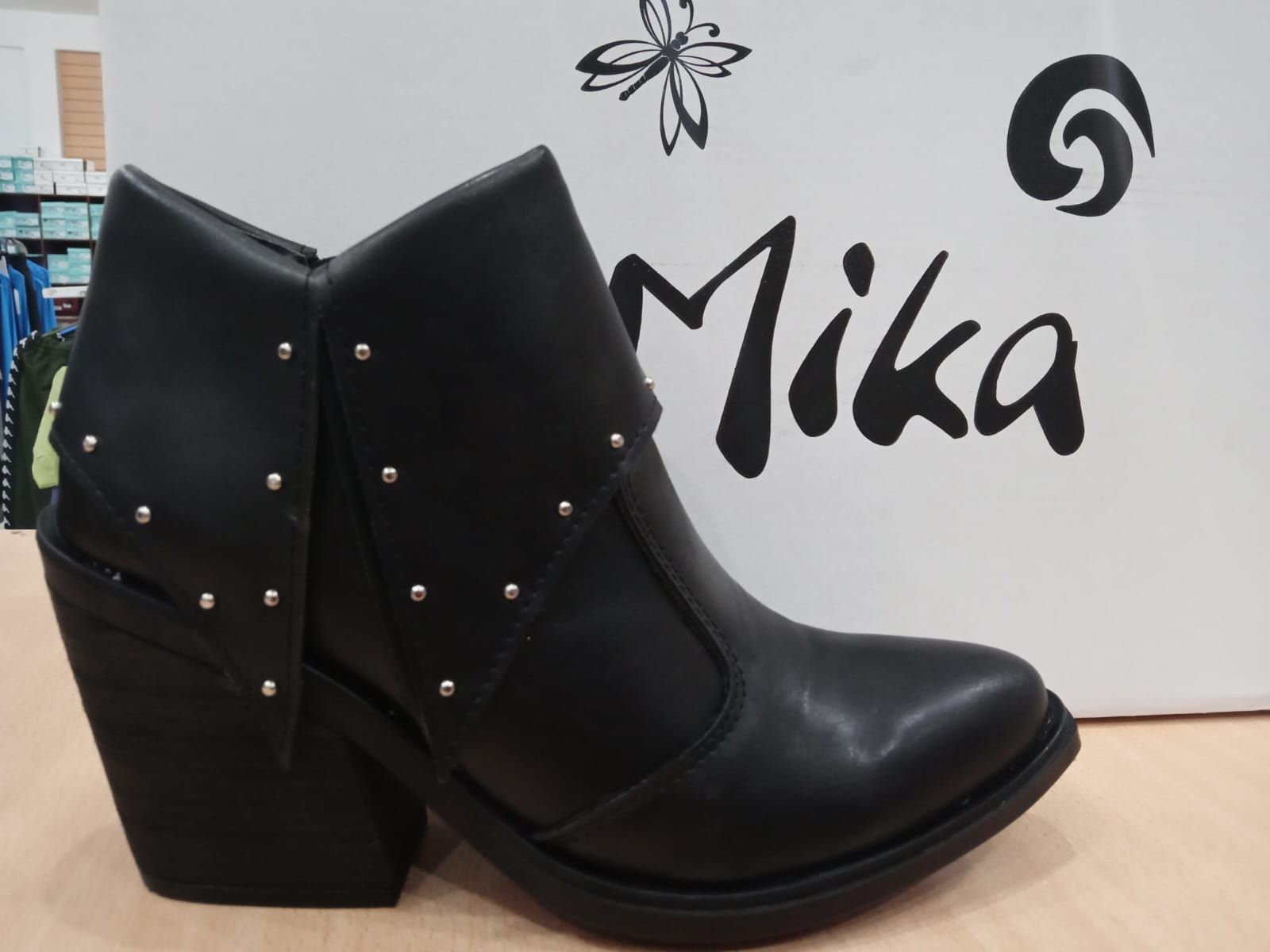Botín negro con tachuelas sobre una superficie blanca con el logotipo de Mika al fondo.