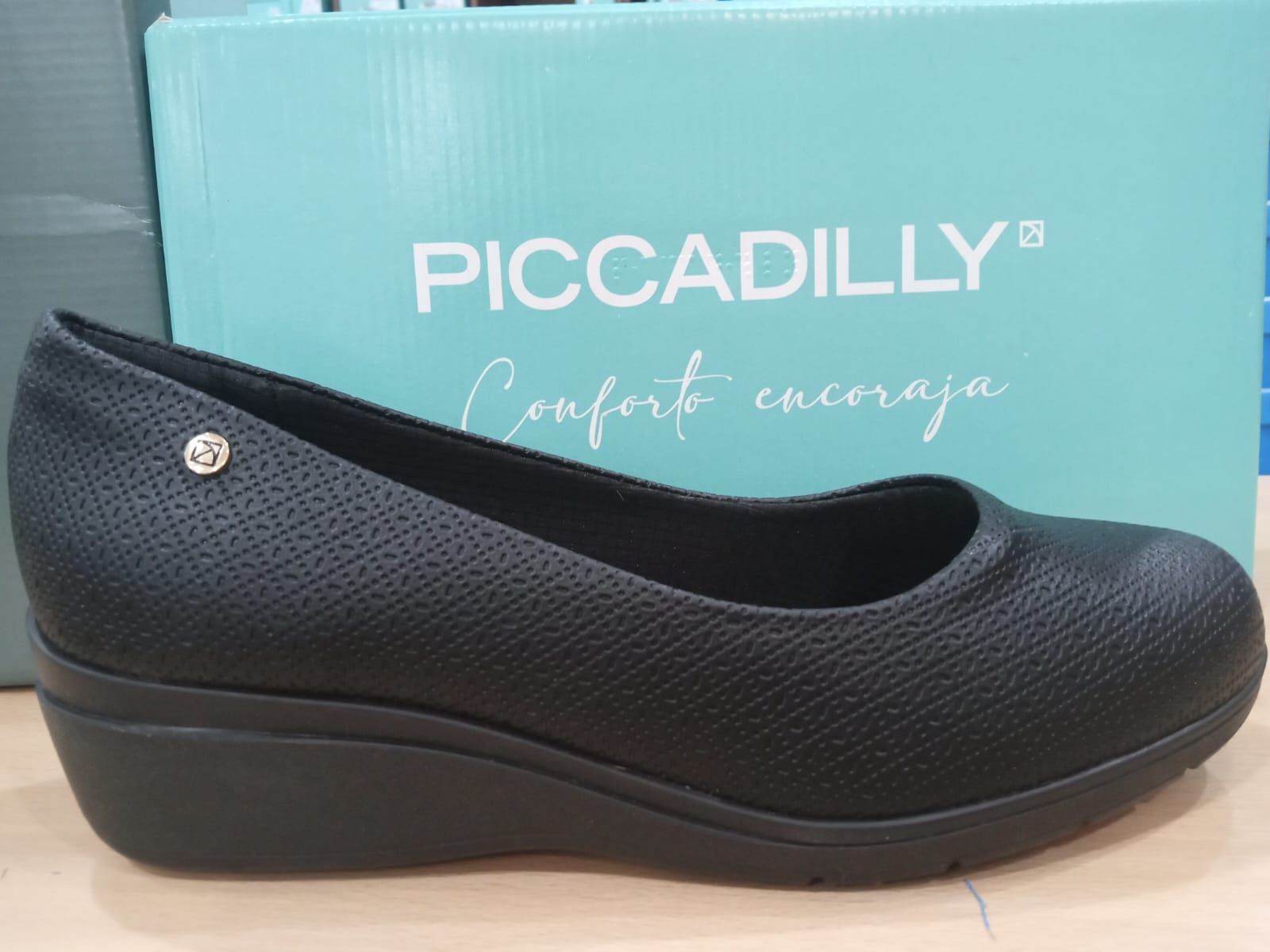 Zapato de cuña Piccadilly negro delante de una caja color turquesa