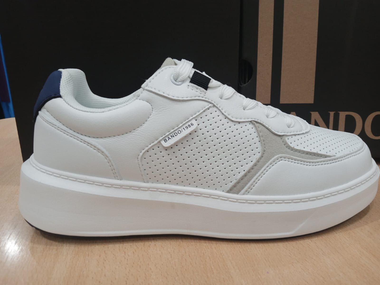 Zapatillas bajas blancas con panel lateral perforado sobre superficie de madera.