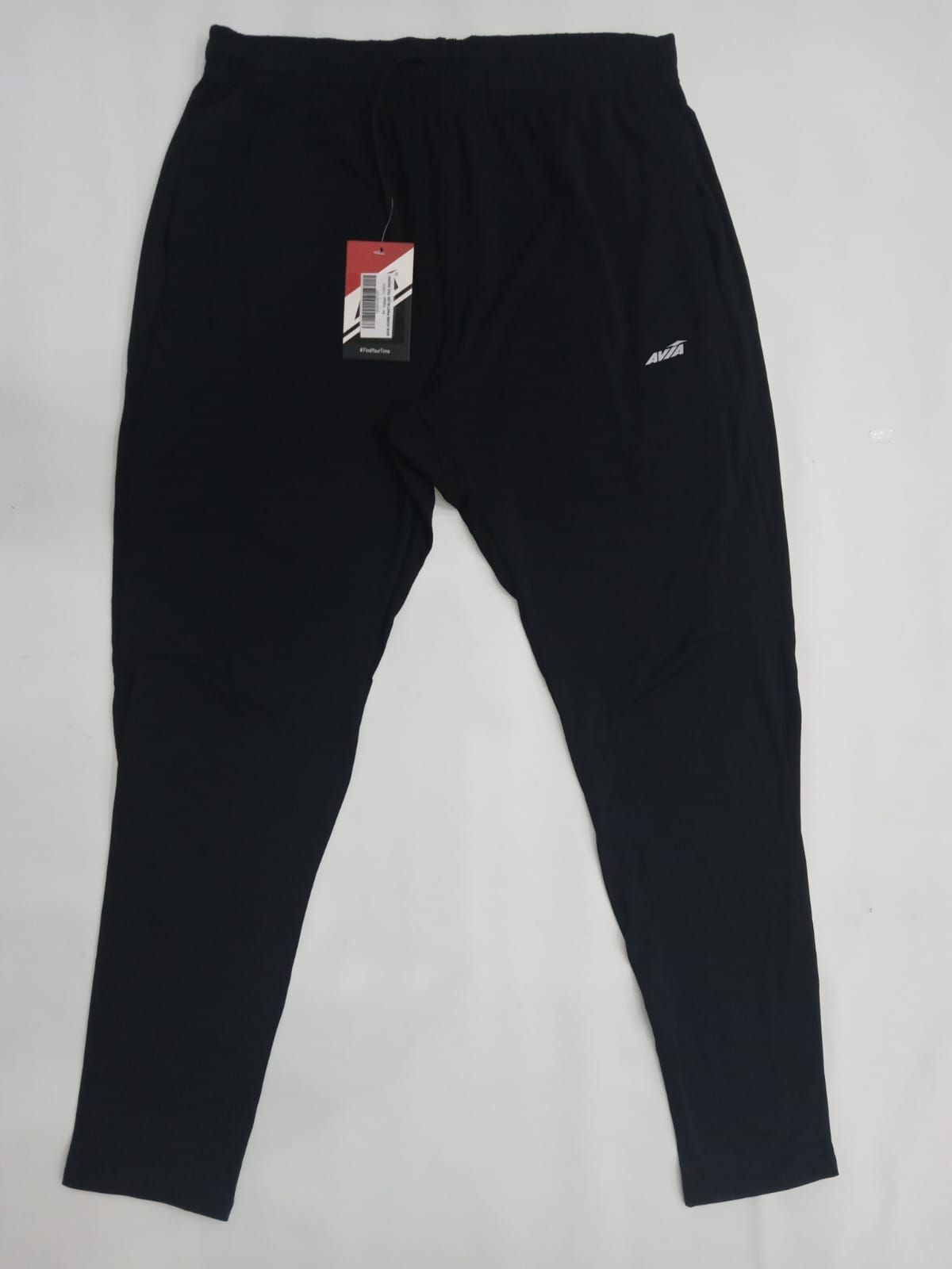 Pantalones deportivos negros extendidos sobre un fondo blanco, con una pequeña etiqueta roja y blanca cerca de la cintura.