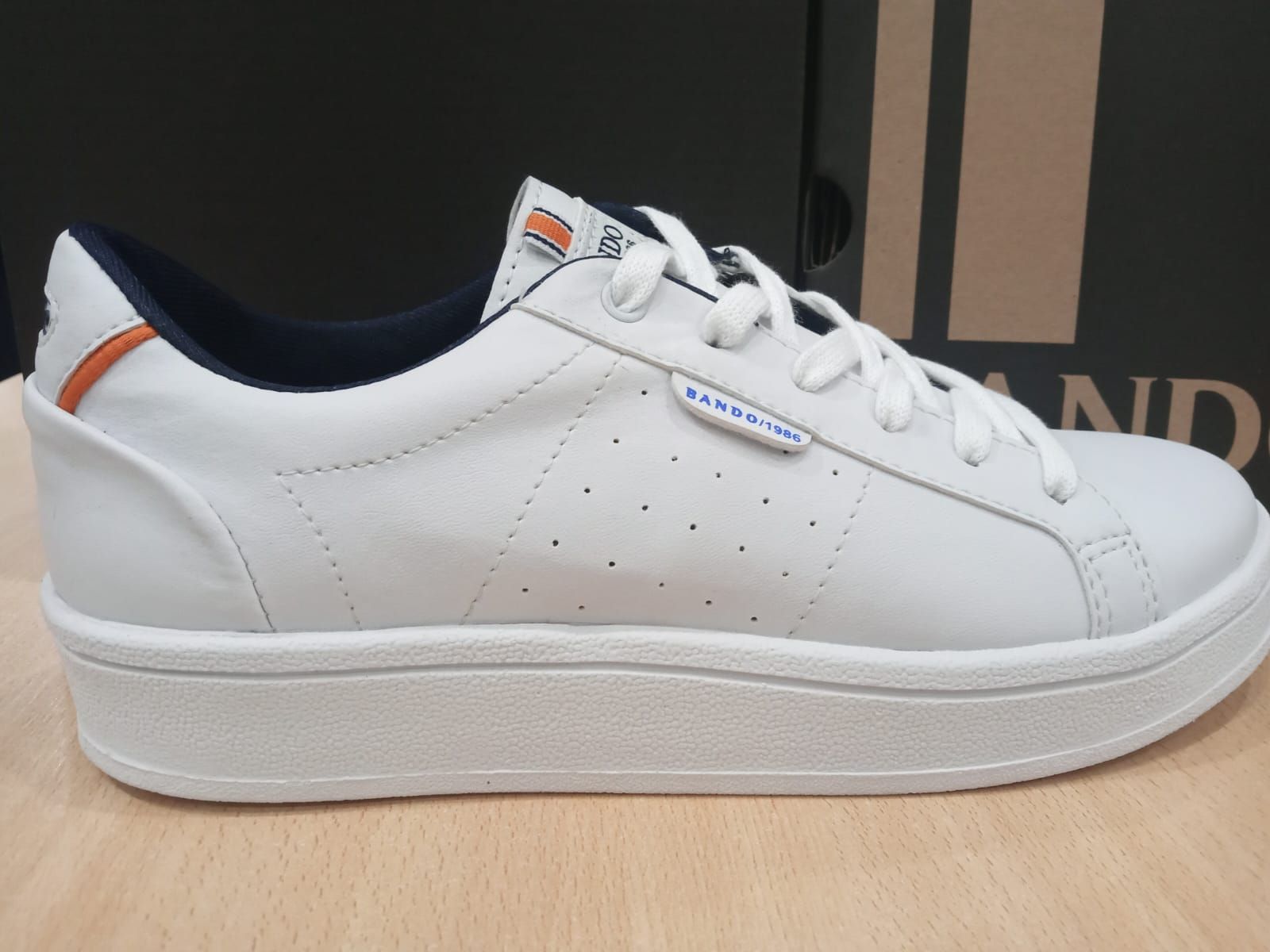 Zapatillas bajas blancas con detalles naranjas sobre fondo liso.