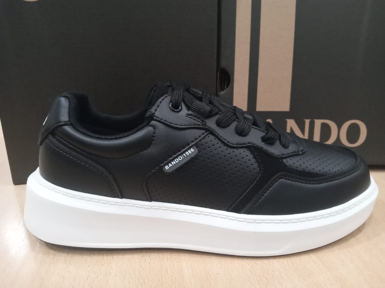 Zapatillas negras con suela de plataforma blanca, vista lateral sobre un fondo de caja.