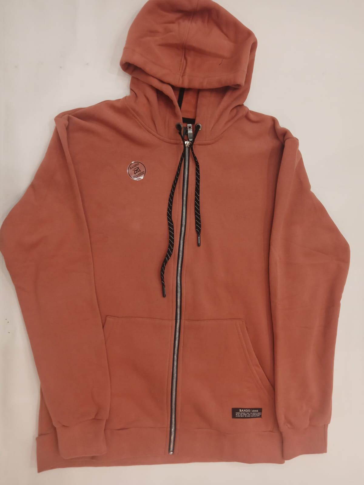 Sudadera con capucha y cremallera de color óxido, con cordones negros, extendida sobre un fondo blanco.