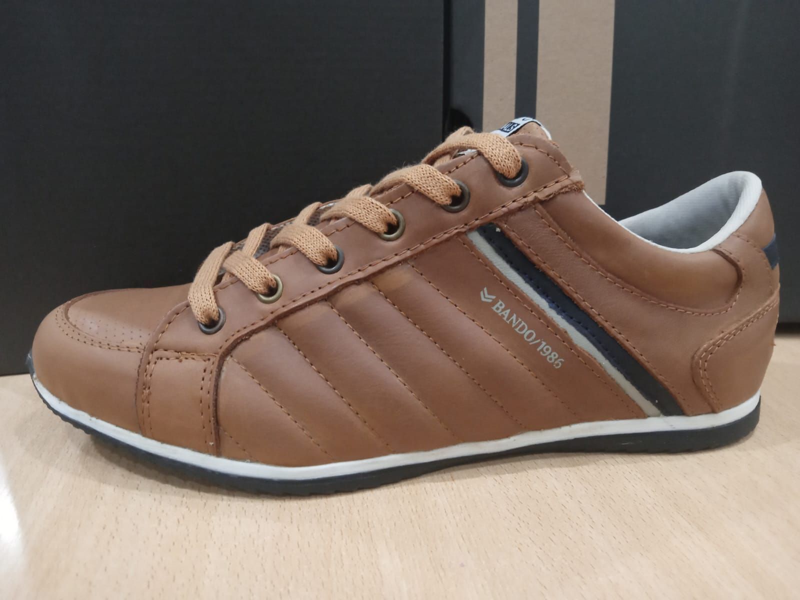 Zapatillas deportivas de piel marrón con cordones color camel y suela blanca, vistas de perfil sobre una superficie clara.