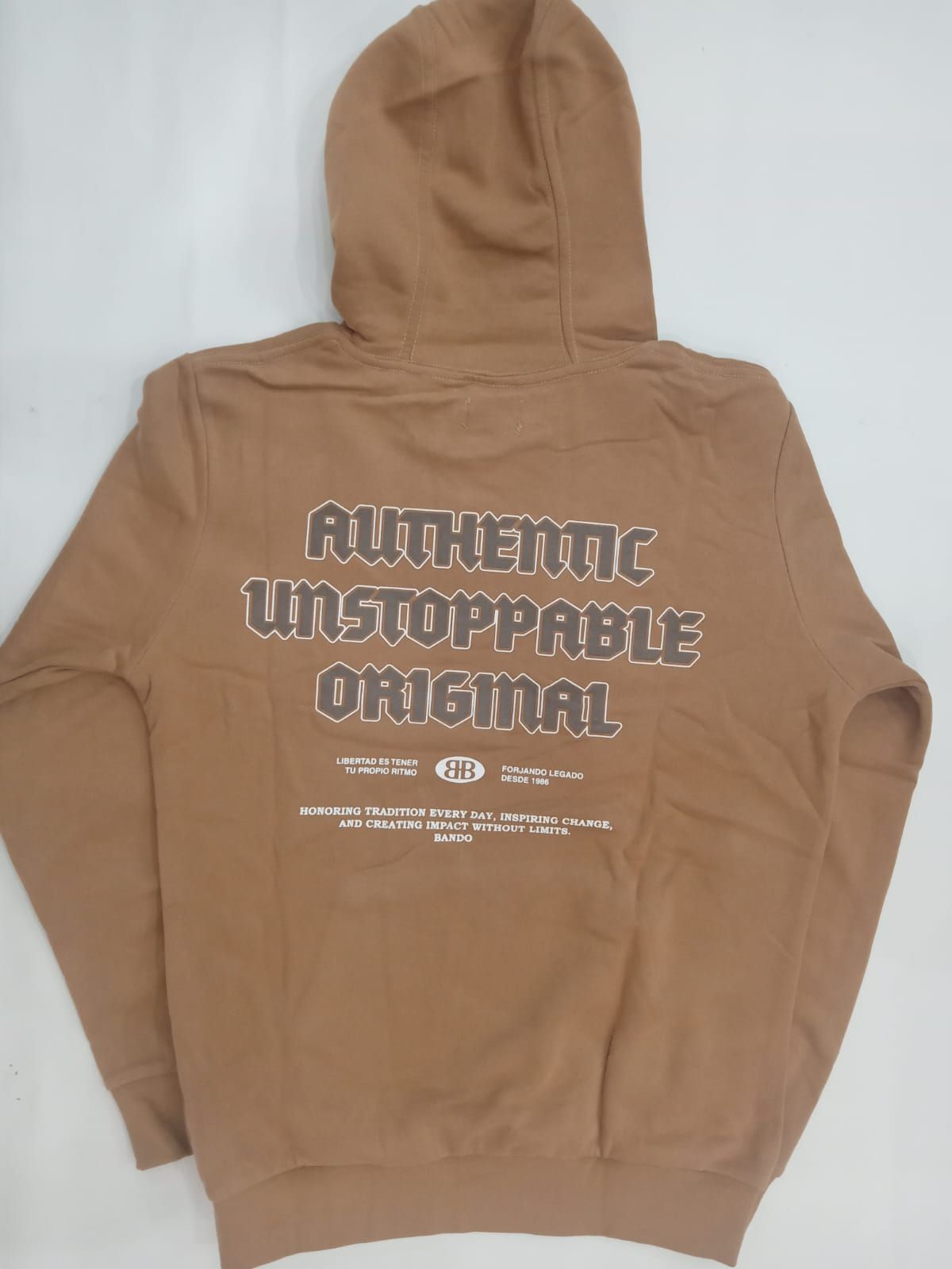 Sudadera marrón con capucha, extendida sobre una superficie plana, con un pequeño gráfico en el pecho y una etiqueta adjunta.