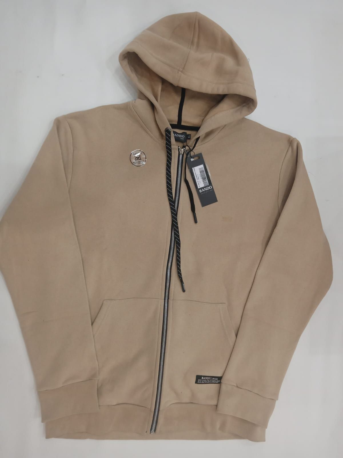Chaqueta con capucha y cremallera color beige, extendida sobre una superficie plana con la etiqueta puesta.