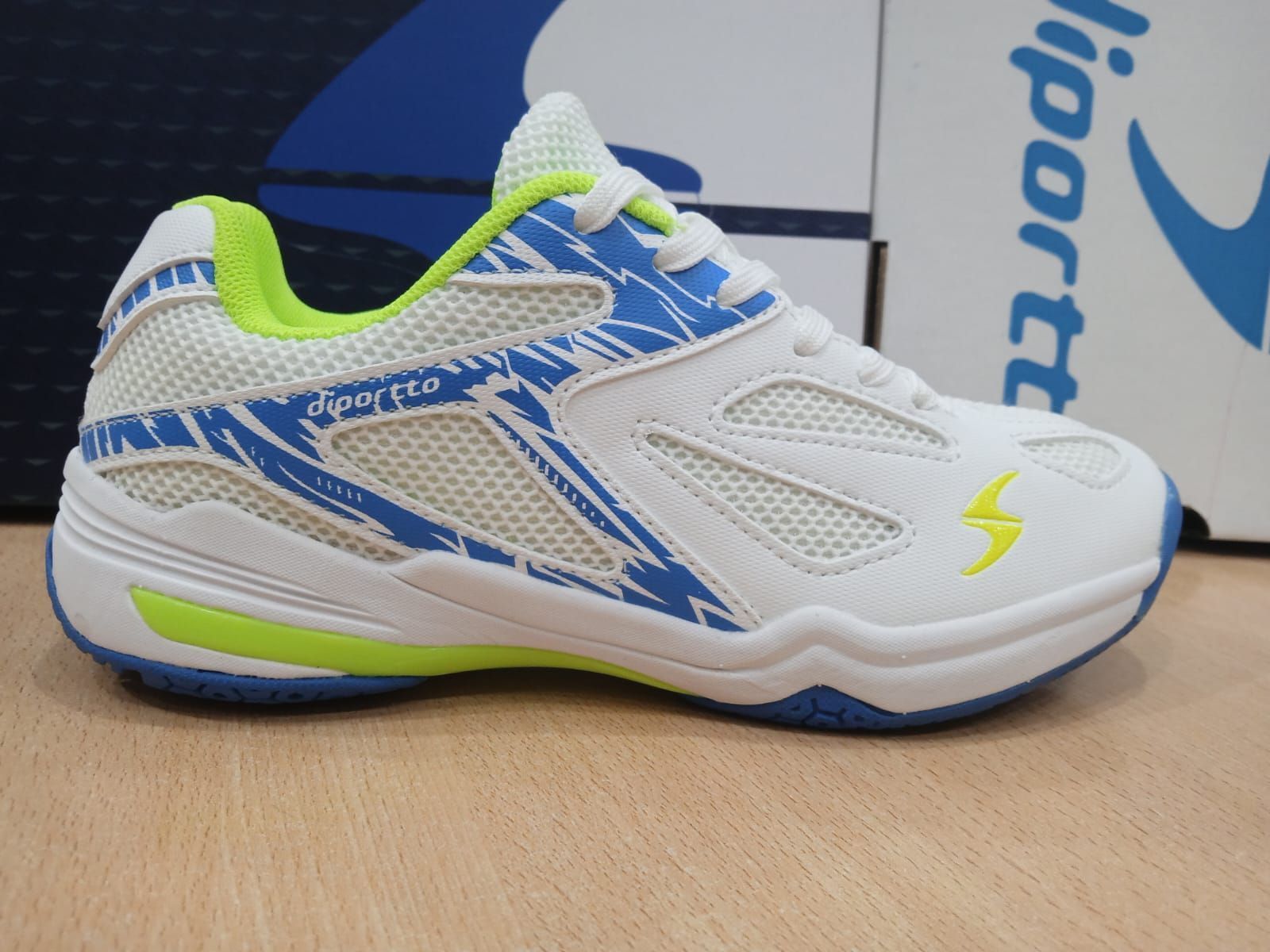 Zapatillas deportivas blancas y azules con detalles en verde neón sobre una mesa de madera.